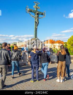 Touristen durch die Skulptur Kruzifix und Golgatha stehend mit hebräischen Text höhnische mittelalterliche jüdische Bürger der Karlsbrücke in Prag in der Tschechischen Republik. Stockfoto
