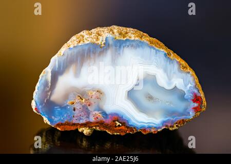 Weiß Blau poliert Achat Edelstein Querschnitt. Reflexion auf farbigem Hintergrund. Einen Quarz Chalcedon detail. Kristalle in einem kleinen Geode. Eis aussehen. Stockfoto