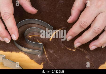 Metall 08/15 auf Lebkuchen Teig detail und weibliche Hände. Schneiden Sie eine hufeisenförmige Weihnachtsstollen aus gewalzten rohen Teig auf Holz. Stockfoto