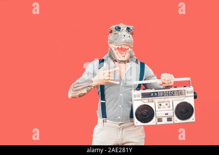 Crazy älterer Mann mit T-rex Maske, während Sie Musik hören, die Vintage boombox stereo Outdoor - Fashion masquerade männlichen Spaß tanzen Stockfoto