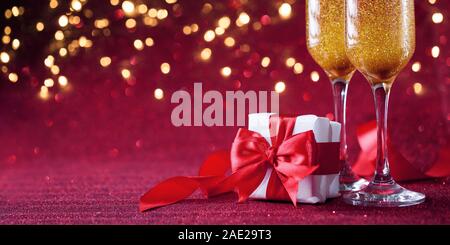 Zwei Gläser Champagner mit Geschenk auf rotem Hintergrund. Romantische Feier der Valentinstag Stockfoto