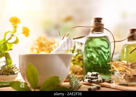 Kapseln und Flaschen von Wesen der natürlichen Medizin mit Heilpflanzen auf hölzernen Tisch in rustikale Küche. Vorderansicht. Horizontale Komposition. Stockfoto
