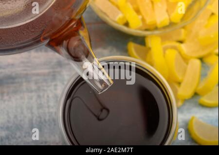 Schwarzer Tee ist aus einer Teekanne in ein Glas gegossen, Marmelade Zitronenscheiben auf einer hölzernen Hintergrund. Nahaufnahme Stockfoto