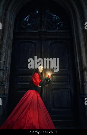 Geheimnisvolle Frau in einem roten Viktorianische Kleid von die alte Tür Stockfoto