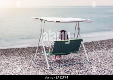 Junge Frau sitzt am Strand bei Sonnenuntergang. Stockfoto
