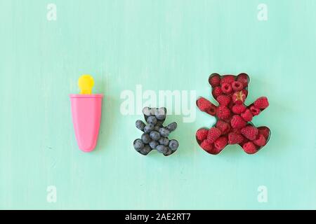 Teddybär geformte Formen für die cookies voller Frische organische Himbeeren und Pink popsicle Form für Sorbet auf Türkisfarbenem Hintergrund. Stockfoto
