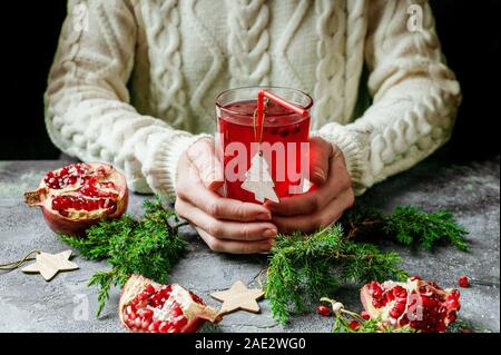 Weibliche Hände halten ein Glas Glühwein mit Granatapfel. Traditionelle Weihnachten Wein trinken. Stockfoto