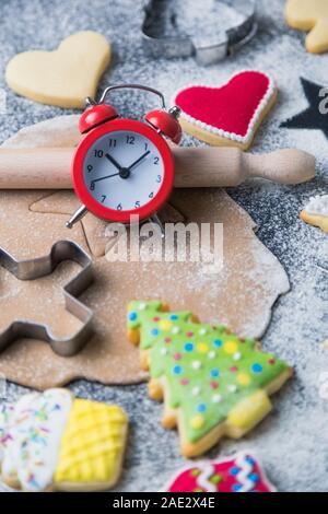 Flach für Weihnachtsplätzchen Vorbereitung Konzept aus Schneider, Teig, Nudelholz, Kekse mit bunten Vereisung und Wecker auf Tisch. Stockfoto