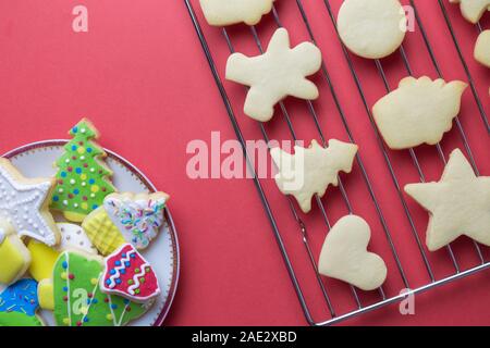 Flach von Weihnachtsplätzchen auf Platte und auf Backofen Gitter mit verzierten Kekse gegen roten Hintergrund minimal kreativ Urlaub und Essen Konzept. Stockfoto