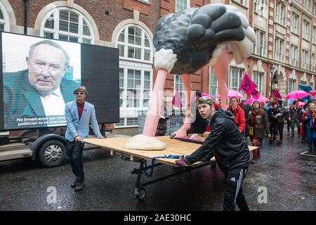 London, Großbritannien. 6. Dezember, 2019. Klimawandel Aktivisten vor dem Aussterben Rebellion ein 4 Meter hohes Strauß zu Dance Party eine "Operation Big Bird' außerhalb der Konservativen Partei bringen als Teil einer Reihe von Protest Wahl Rebellion bestimmt sind." Der Druck auf die politischen Parteien, die Klima und ökologische Not in den Mittelpunkt ihrer allgemeinen Wahlkampf zu platzieren. Ein Bildschirm auf die Website von Aktivist Gruppe von Eseln Relais Andrew Neil's Herausforderung an Boris Johnson für ein Interview im Hintergrund zu sorgen LED-gebracht. Credit: Mark Kerrison/Alamy leben Nachrichten Stockfoto