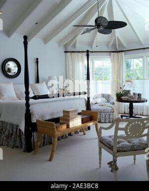 Elektrische Decken Ventilator in einem hellen und luftigen Schlafzimmer mit einem weissen Teppich und ein antikes Bett mit gedrehtem Holz- spindeln Stockfoto
