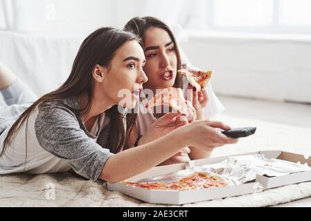 Keine Möglichkeit, haben Sie gesehen. Schwestern essen Pizza beim Fernsehen, während auf dem Boden des schönen Schlafzimmer tagsüber liegen Stockfoto