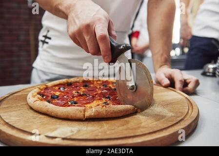 Mit speziellen Gerät zum Schneiden. Bild von bereit, leckere Pizza mit Würstchen Ringe und Oliven Stockfoto