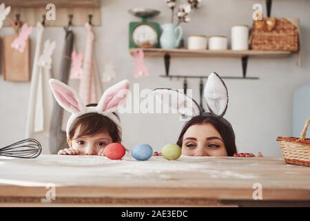 Versteckt in der Nähe des Tisches. Mutter und Tochter im bunny Ohren zu Ostern haben Sie etwas Spaß in der Küche tagsüber Stockfoto