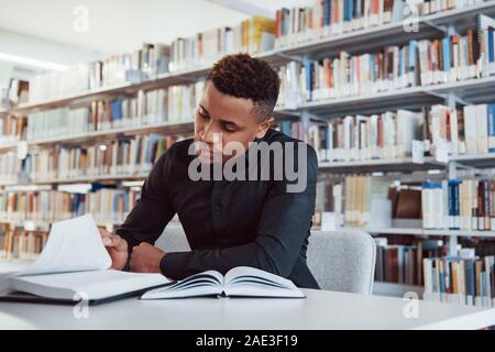 Afrikanische amerikanische Mann sitzt in der Bibliothek und auf der Suche nach einige Informationen in der Bücher Stockfoto