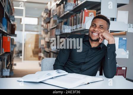 Zeit für den Rest. Afrikanische amerikanische Mann sitzt in der Bibliothek und auf der Suche nach einige Informationen in der Bücher Stockfoto