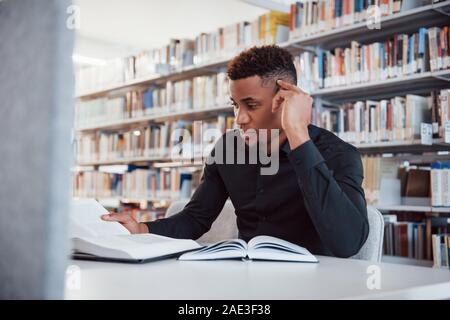 Durch die Suche recht müde. Afrikanische amerikanische Mann sitzt in der Bibliothek Stockfoto