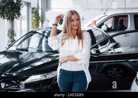 In Jeans und weißem T-Shirt. Junge Manager im Auto Shop steht gegen perfekt poliert schwarzes Auto Stockfoto