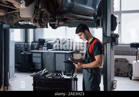 Blick von der Seite. Menschen, die auf dem Workshop in Uniform mit Notepad für seinen Job zur Befestigung gebrochen Auto Stockfoto