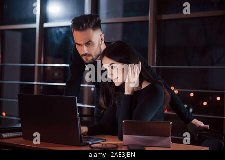 Steht hinter der Frau. Team der jungen Unternehmer arbeitet an ihrem Projekt in der Nacht im Büro Stockfoto