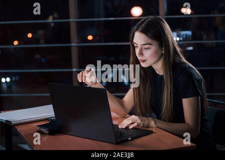 Viele der Arbeiten, die sie haben. Attraktive brünette Geschäftsfrau arbeitet allein im Büro bei Nacht Stockfoto