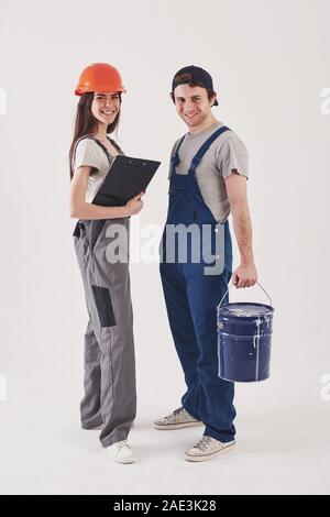 Zusammen zu arbeiten. Mann in der blauen Uniform mit Frau in harten Hut steht vor weißem Hintergrund im Studio Stockfoto