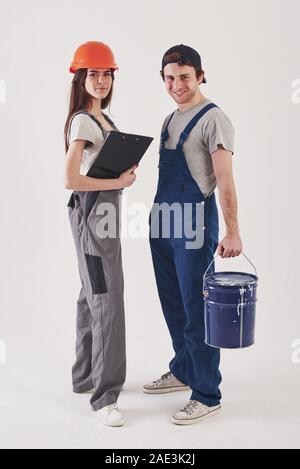 Zwei Mitarbeiter. Mann in der blauen Uniform mit Frau in harten Hut steht vor weißem Hintergrund im Studio Stockfoto