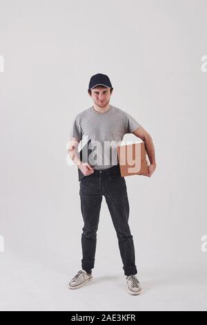 Die Ernte der Bestellung. Kerl mit Box in den Händen steht vor weißem Hintergrund im Studio Stockfoto