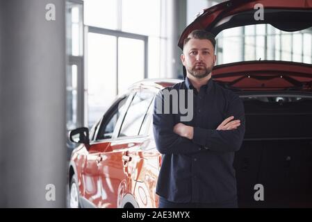 Tagsüber. Vorderansicht des junge Bartgeier Geschäftsmann steht in der Nähe von seiner luxuriösen rotes Auto Stockfoto