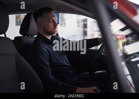 In dem schwarzen T-Shirt. Seitenansicht der junge Bartgeier Geschäftsmann, der in seiner luxuriösen rotes Auto sitzen Stockfoto
