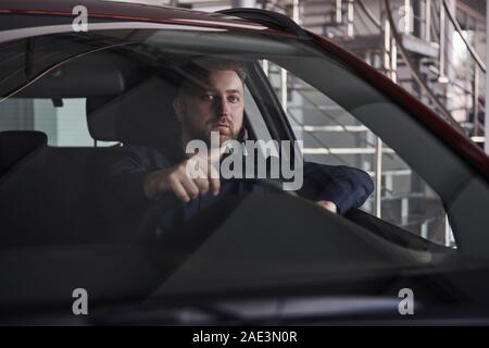Modern aussehende Kerl. Vorderansicht des junge Bartgeier Geschäftsmann, der in seiner luxuriösen rotes Auto sitzen Stockfoto
