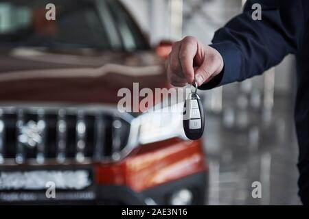 Nahaufnahme der Hand Mann hält den Schlüssel von neuen roten Auto, das im Hintergrund steht Stockfoto