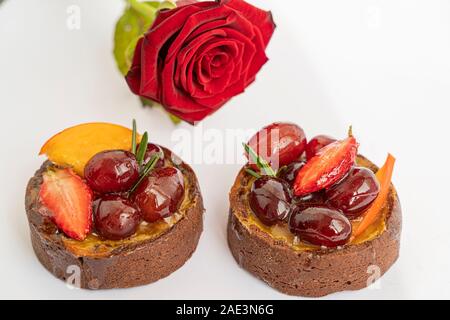 Zwei leckere Schokolade Kuchen mit Puderzucker Früchte und Beeren auf weißem Hintergrund mit roten Rose, isoliert und Makro. Romantische Dessert. Stockfoto