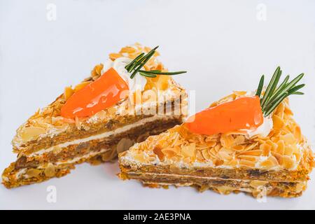 Zwei Stück Karottenkuchen ausgebaggert mit gehobelten Mandeln und mit natürlichen Karotte auf weißem Hintergrund isoliert und Nahaufnahme. Natürliche Süßigkeiten Konzept Stockfoto