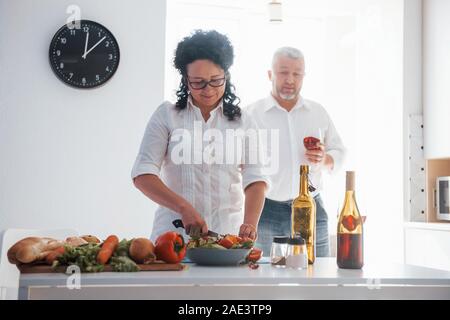 Versucht, für ihren Mann. Der Mensch und seine Frau in weißem Hemd die Zubereitung von Speisen in der Küche mit Gemüse Stockfoto