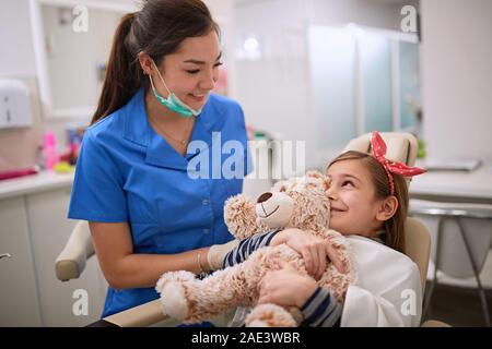 Junge Mädchen umarmt Teddybär und weiblichen Zahnarzt Stockfoto
