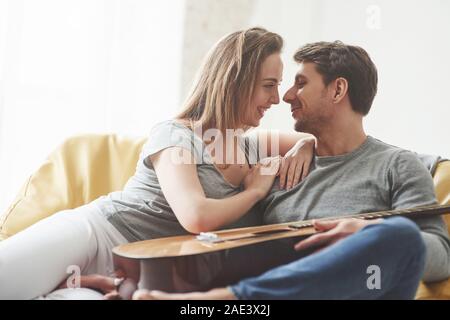 Singt mir das Lied. Gitarre auf die Beine. Glückliches Paar entspannende auf dem gelben Sofa im Wohnzimmer ihres neuen Hauses Stockfoto