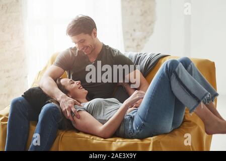 Schönen Sonnenlicht, das aus dem widnow. Glückliches Paar entspannende auf dem gelben Sofa im Wohnzimmer ihres neuen Hauses Stockfoto