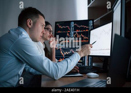 Am Abend Zeit arbeiten. Mannschaft der Börsenmakler sind ein Gespräch in einem Büro mit mehreren Bildschirmen Stockfoto