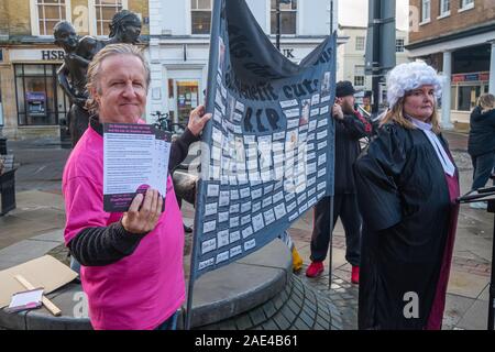 London, Großbritannien. 6. Dezember 2019. Die Menschen halten ein Banner Benennung von ein paar von denen, die wegen der Leistungskürzungen und Sanktionen gestorben sind. Ein straßentheater Versuch durch behinderte Menschen gegen Sozialabbau (DPAC) im Zentrum von Uxbridge fordert Wähler Boris Johnson und die Tories abzulehnen. Sie verweisen auf die geschätzten 200.000 vorzeitige Todesfälle durch Kürzungen und Sanktionen einschließlich der Beseitigung der Independent Living Fund, zu Universal Kredit, zu einem enormen Anstieg der Foodbank verwenden, Hunger, Verschuldung und Zwangsräumungen und ein UN-Bericht "ernste und systematische Verletzungen der Rechte behinderter Menschen geführt hat. Peter Marshall / ALAMY L Stockfoto