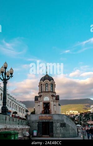 Jalta, Crimea-October 9, 2019: Kapelle zu Ehren des heiligen Alexander Newski in Jalta. Warme, sonnige Herbst am Abend bei Sonnenuntergang. Menschen gehen am Wasser. Stockfoto