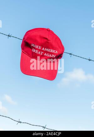 Donald Trump Anhänger rot MAGA Kampagne Hut/Kappe auf Stacheldraht + blue sky. Metapher Trumpf US-Einwanderungspolitik, Trumpf Grenzmauer. Stockfoto