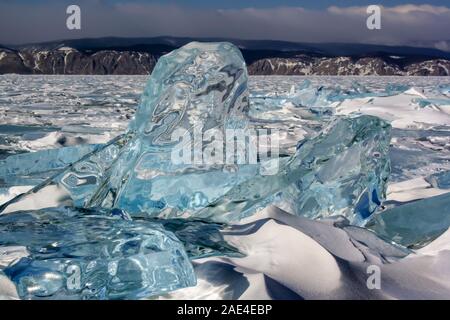 Große gefrorene Eis am Baikalsee von der Sonne geschmolzen. Reflexionen und Verzerrungen in durchsichtigen Eis. Viele gebrochene Eis rund um. Berge auf Stockfoto