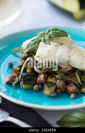 Pochierter Fisch über Ratatouille mit Kapern und Basilikum Stockfoto