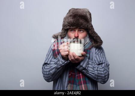 Menschen leiden an einer Grippe mit Schlafanzug und mit einer Kappe weht eine heiße Tasse Tee auf einem grauen Hintergrund zu warm. Gesundheit Konzept. Stockfoto