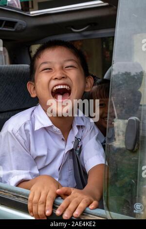 Die jungen Burmesischen boy brüllt vor Lachen, während Sie in einem Bus sitzen und schauen aus dem Fenster in Homalin, Myanmar (Birma) Stockfoto