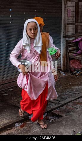 Buddhistische Nonnen durch einen Markt mit ihren Almosen Schalen auf der Suche nach Spenden während ein heiliger Tag in Mandalay, Myanmar (Birma) Stockfoto