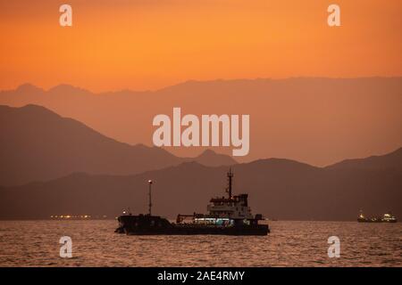 Sonnenuntergang von Lamma Island in Hongkong als lokale Schiffe in Richtung Hafen Aberdeen Stockfoto