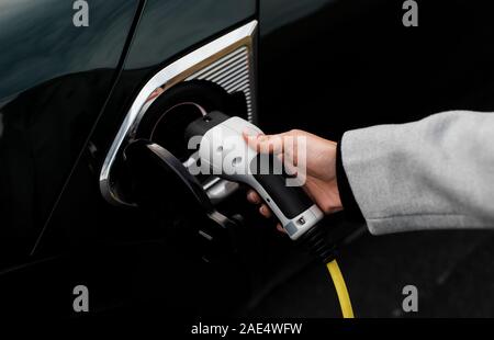 Frau Hand und Buchse einstecken in ein elektrisches Auto Stockfoto