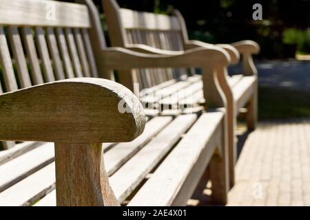 In der Nähe von zwei Holz- classic Teak Bänke in der Sonne im Sommer mit selektiven Fokus auf einer Armlehne Stockfoto